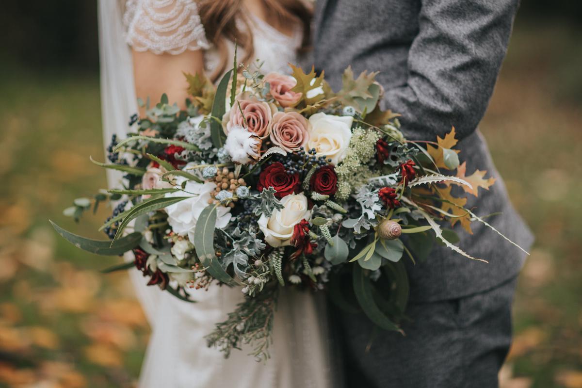 Bride and groom holding wedding bouquet in autumn