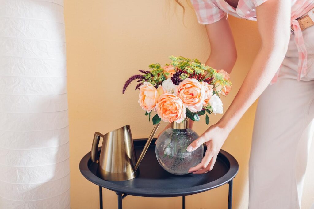 Woman puts vase with bouquet of flowers on table at home.